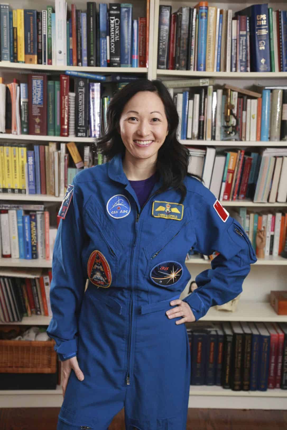 Professional headshot of Julielynn Wong in blue flight suit standing before bookshelf