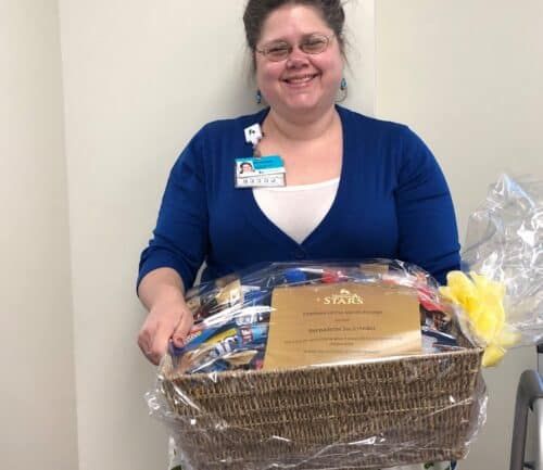 Healthcare employee holding gift basket with Employee of the Month certificate