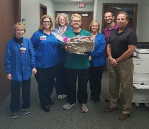 Healthcare staff presenting gift basket to male employee in hospital hallway