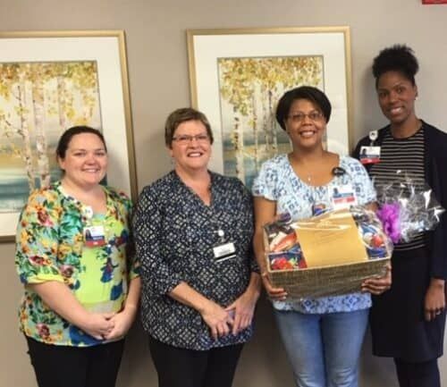 Four healthcare staff members celebrating with gift basket presentation in office setting