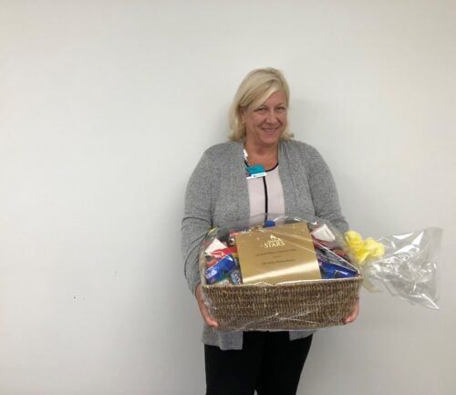Woman in gray cardigan holding wicker gift basket filled with various items