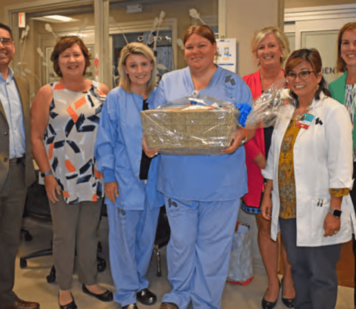 Healthcare team celebrating with nurse holding gift basket in hospital hallway