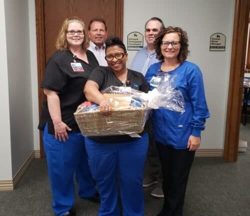 Healthcare team presenting gift basket to employee in hospital hallway