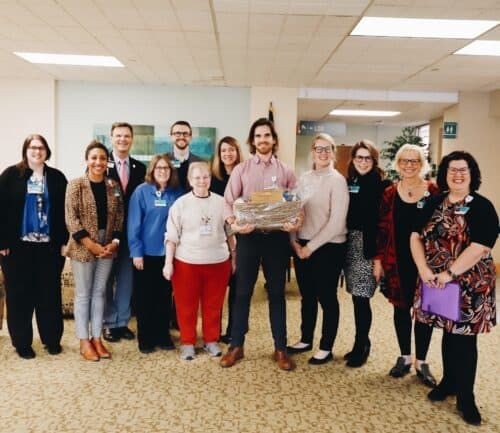 Group of healthcare professionals posing together in hospital lobby, one holding gift basket
