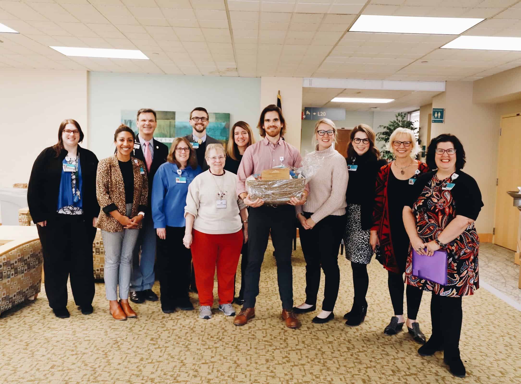 Group of healthcare professionals posing together in hospital lobby, one holding gift basket