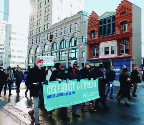 Group marching with "Celebrate the Dream Martin Luther King Jr. Day" banner on snowy street