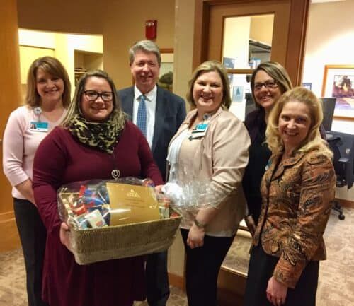 Healthcare team presenting gift basket to woman in burgundy sweater holding award