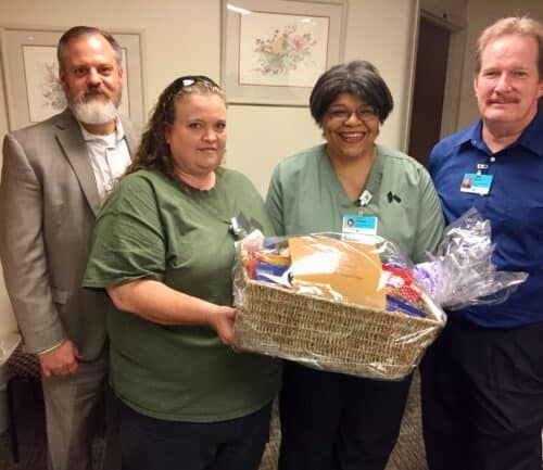 Four healthcare professionals presenting gift basket to two employees in medical scrubs