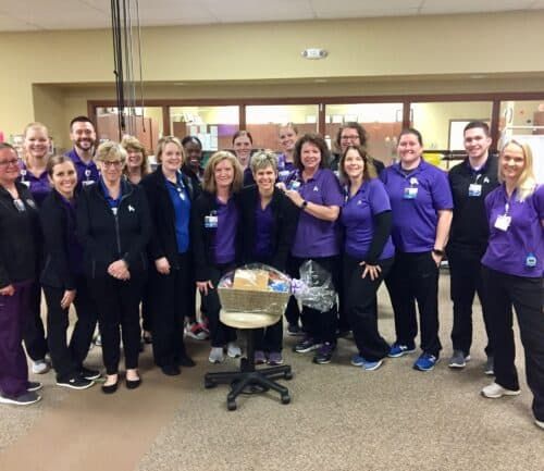 Healthcare team in purple uniforms celebrating employee of the month with gift basket
