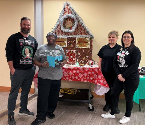 Kettering Health Dayton's Nutrition Services team posing for a picture in front of a decorated gingerbread house