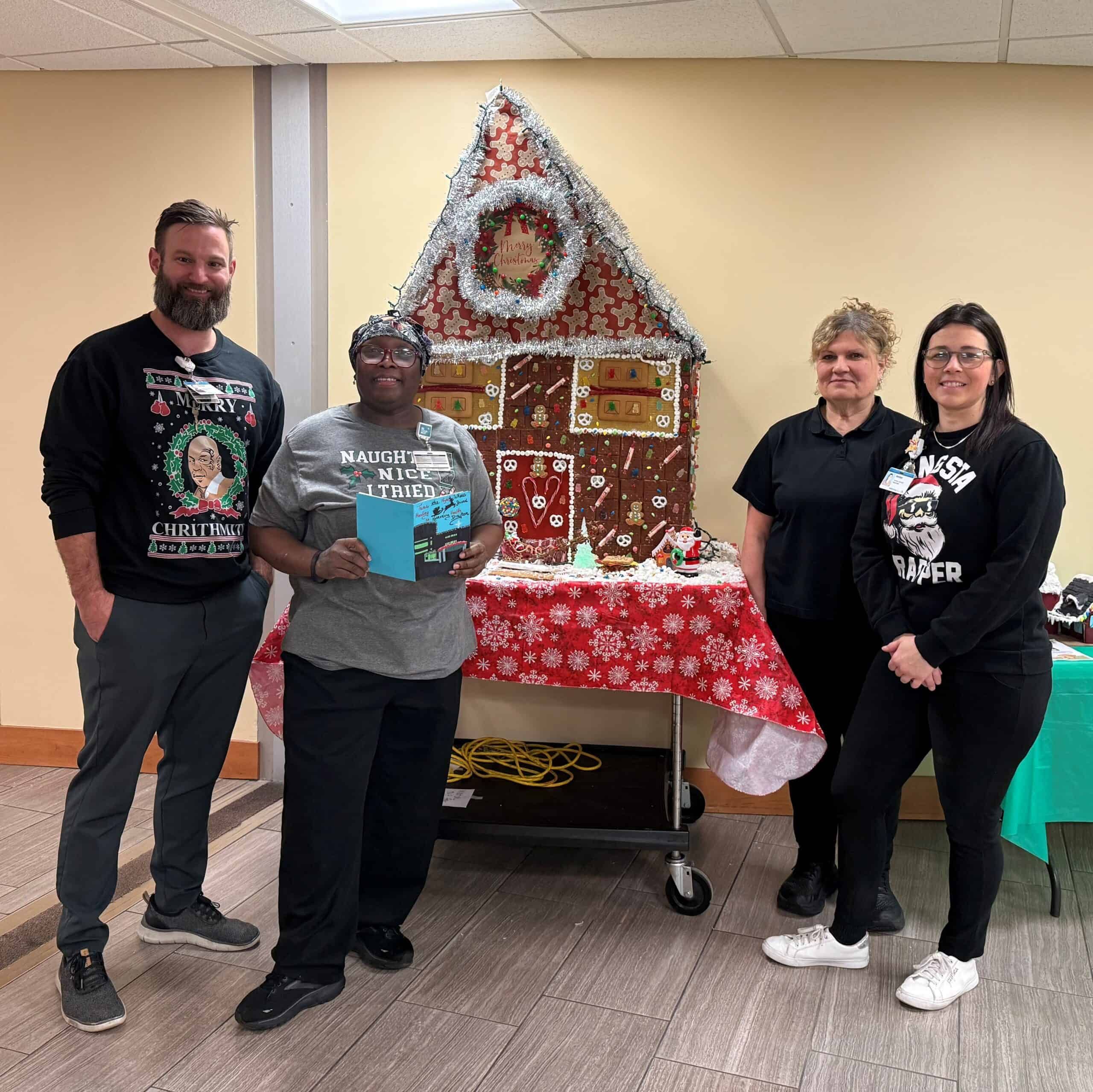 Kettering Health Dayton's Nutrition Services team posing for a picture in front of a decorated gingerbread house