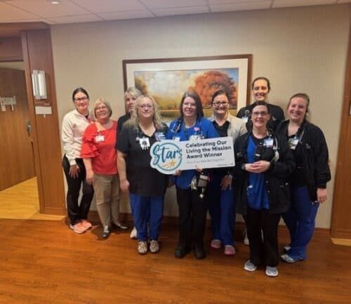 Healthcare staff celebrating with "Living the Mission" award banner in hospital hallway