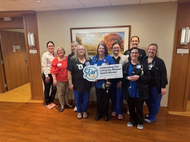 Healthcare staff celebrating with "Living the Mission" award banner in hospital hallway