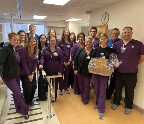 Healthcare team in purple scrubs celebrating with gift basket in hospital hallway