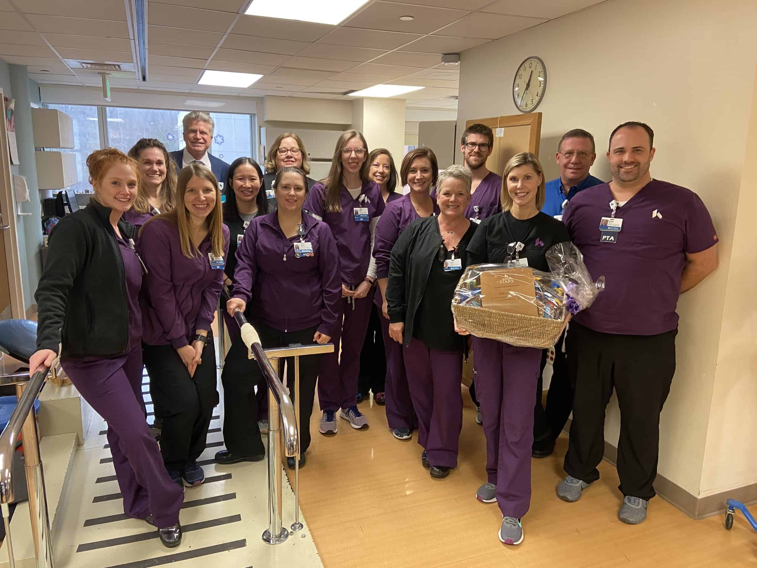 Healthcare team in purple scrubs celebrating with gift basket in hospital hallway