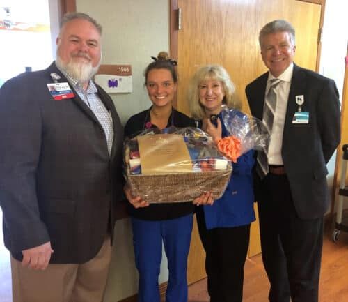 Four people posing together, two women in scrubs holding gift basket with two men in suits