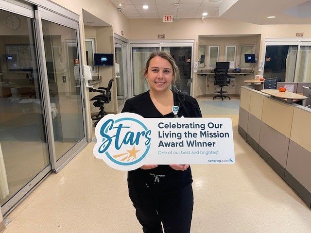 Katie Carroll stands holding a "Living the Mission" sign