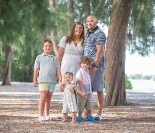 Family of five posing together outdoors under trees in park setting