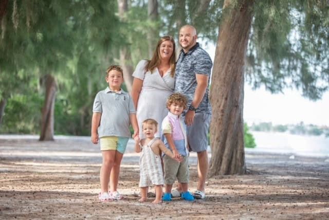 Family of five posing together outdoors under trees in park setting