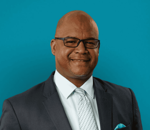 Professional headshot of Keith Jenkins in dark suit against teal background