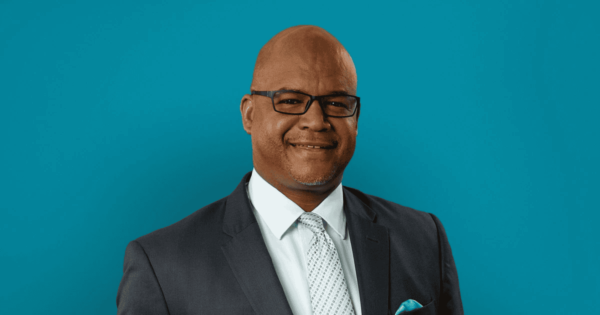Professional headshot of Keith Jenkins in dark suit against teal background