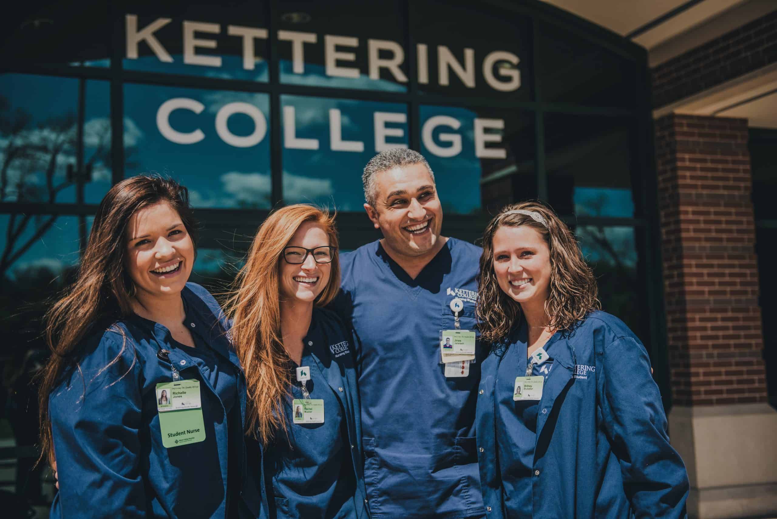 Four nursing students and instructor in blue scrubs smiling outside Kettering College building