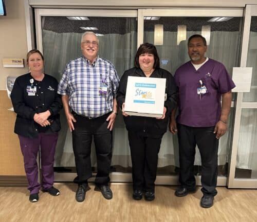 Four healthcare workers celebrating with "Let's Celebrate! Stars" recognition certificate in hospital hallway