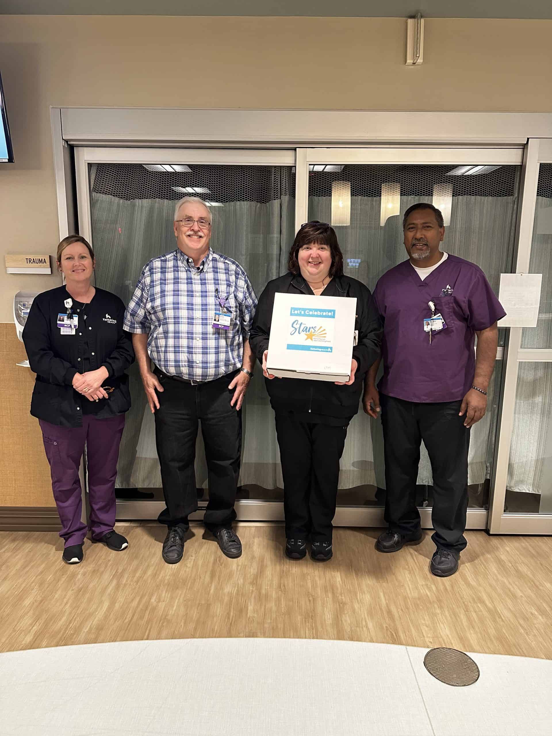 Four healthcare workers celebrating with "Let's Celebrate! Stars" recognition certificate in hospital hallway