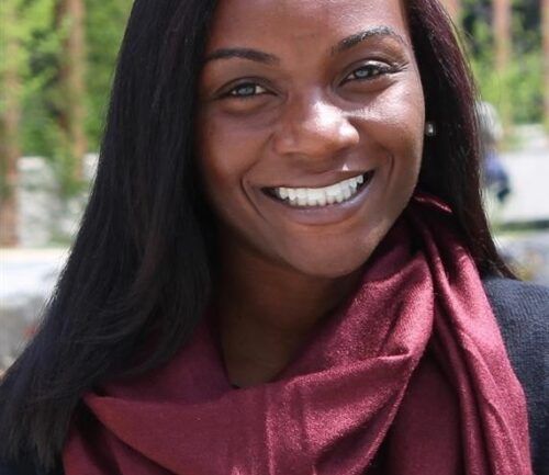 Professional headshot of Kizzy smiling warmly while wearing a burgundy scarf