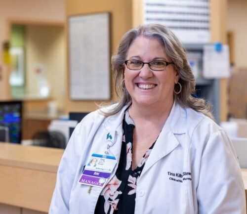 Smiling female healthcare manager in white coat standing at hospital reception desk