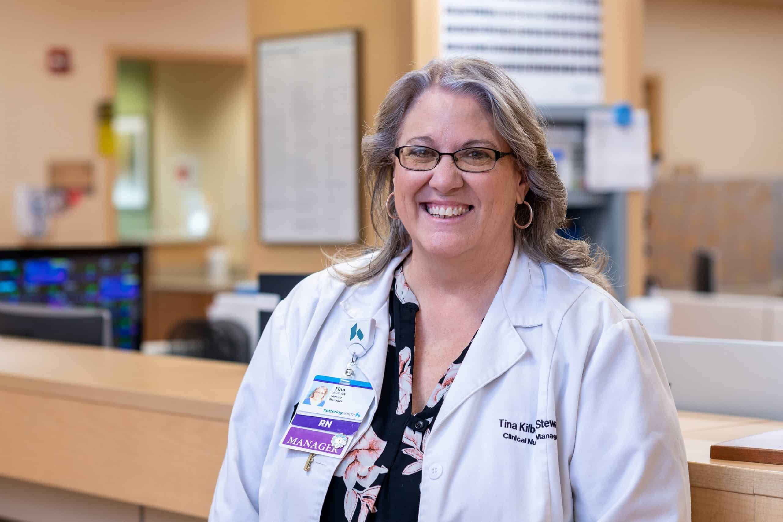 Smiling female healthcare manager in white coat standing at hospital reception desk