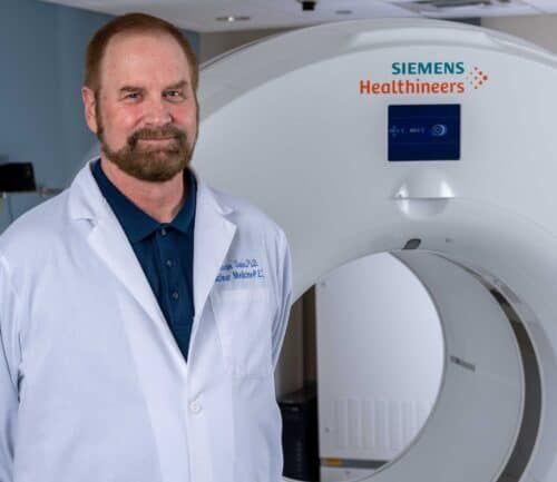 Doctor in white coat standing beside Siemens Healthineers MRI machine