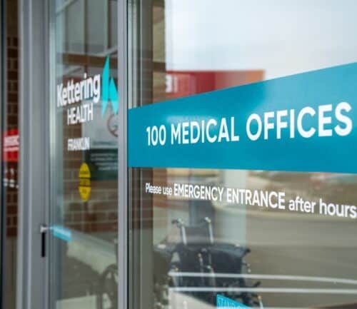 Glass entrance doors to Kettering Health medical offices building with emergency entrance signage.
