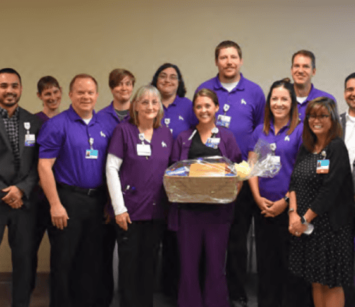 Healthcare team in purple shirts celebrating with gift basket and flowers