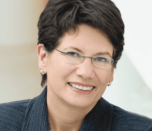 Professional headshot of smiling woman in dark business suit with glasses