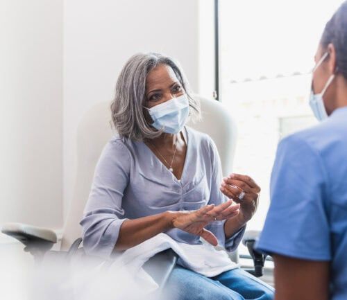 Senior woman in mask consulting with healthcare provider in medical office