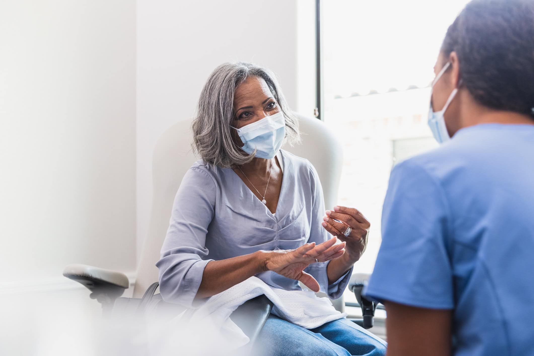 Senior woman in mask consulting with healthcare provider in medical office