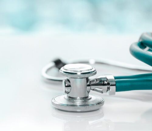 Teal stethoscope with chrome chest piece on white surface with cloudy sky background