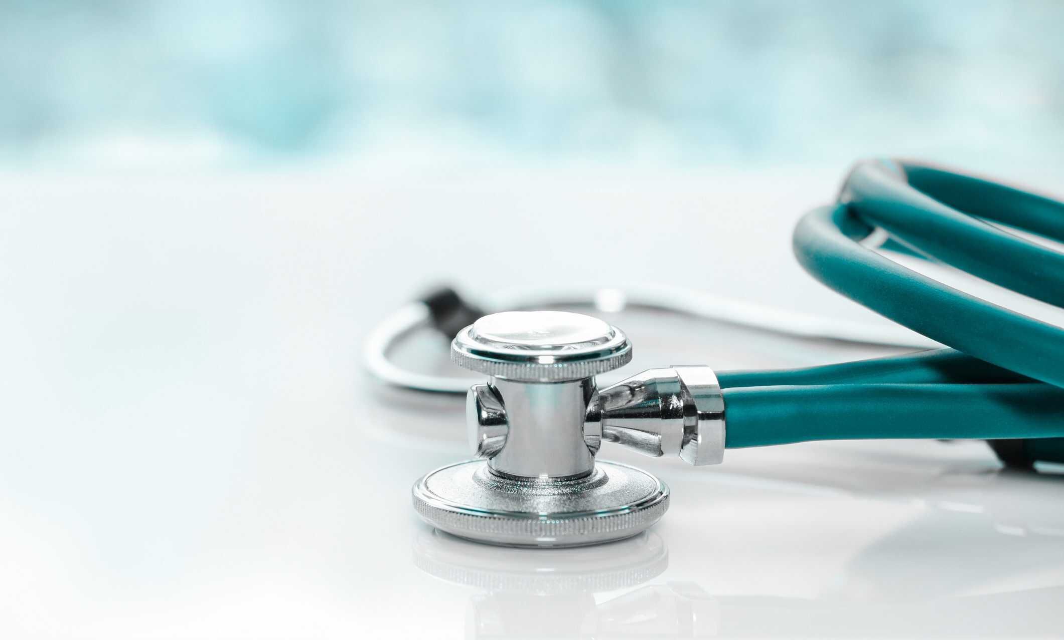 Teal stethoscope with chrome chest piece on white surface with cloudy sky background