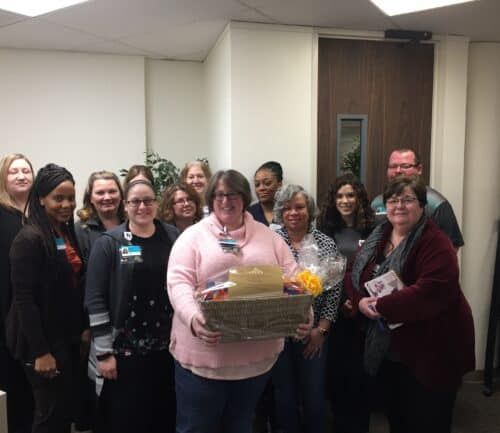 Healthcare team celebrating with coworker holding gift basket in office setting