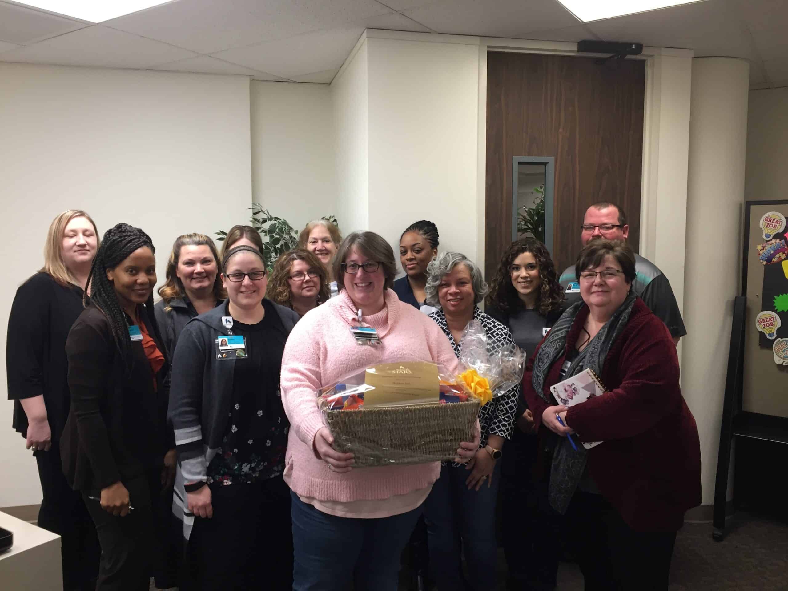 Healthcare team celebrating with coworker holding gift basket in office setting