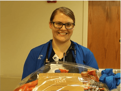 Healthcare worker in blue scrubs smiling while holding packaged medical supplies