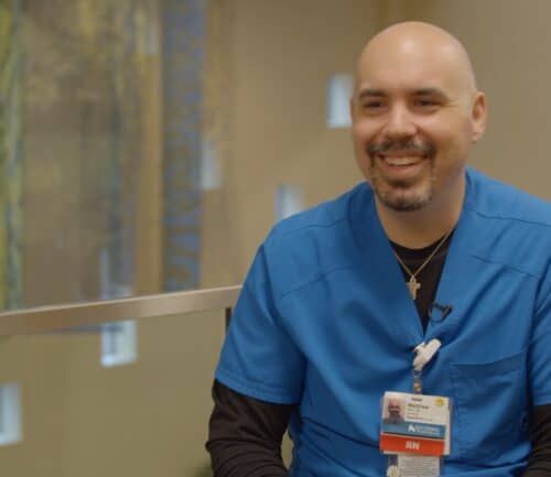 Healthcare professional in blue scrubs smiling while sitting in modern hospital lobby