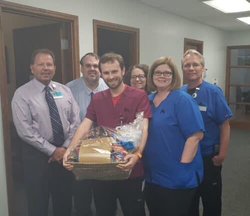 Healthcare staff presenting gift basket to smiling employee in hospital hallway