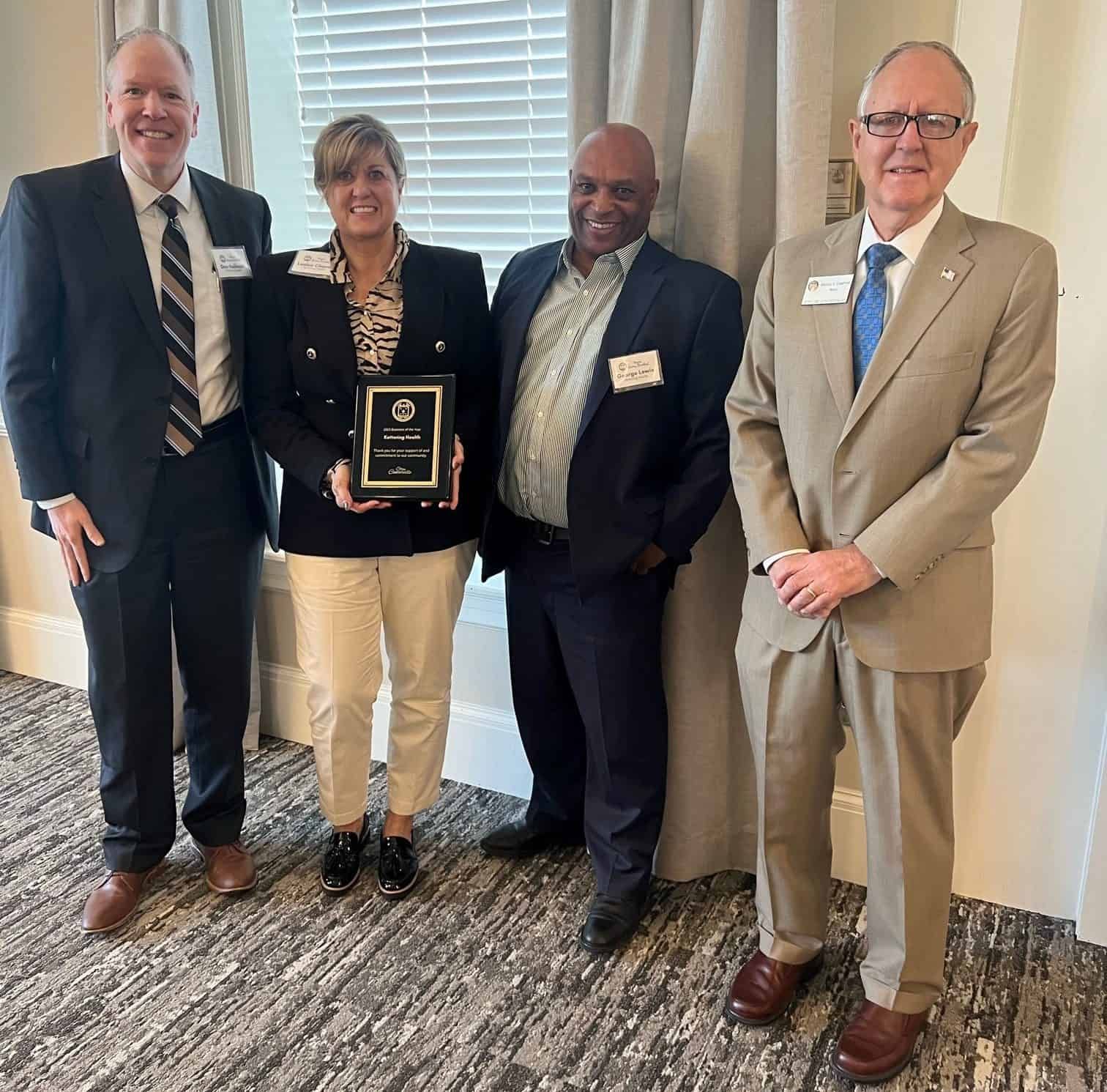 Four business professionals pose together, woman holding award plaque at formal ceremony