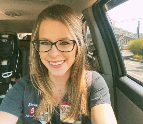 Smiling healthcare worker taking selfie in car wearing Sinclair Nursing uniform