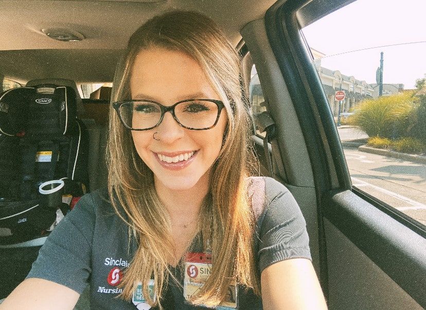 Smiling healthcare worker taking selfie in car wearing Sinclair Nursing uniform