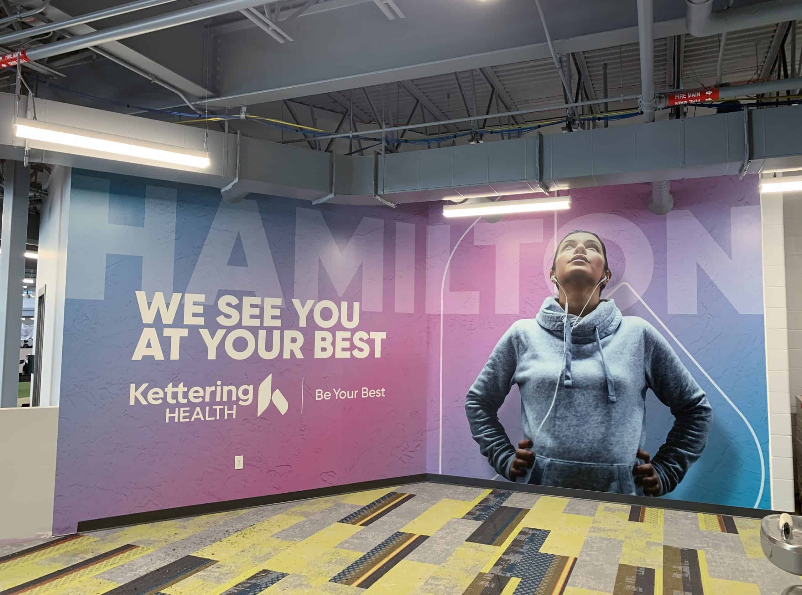 Kettering Health wall mural featuring woman in hoodie with "We See You At Your Best" message