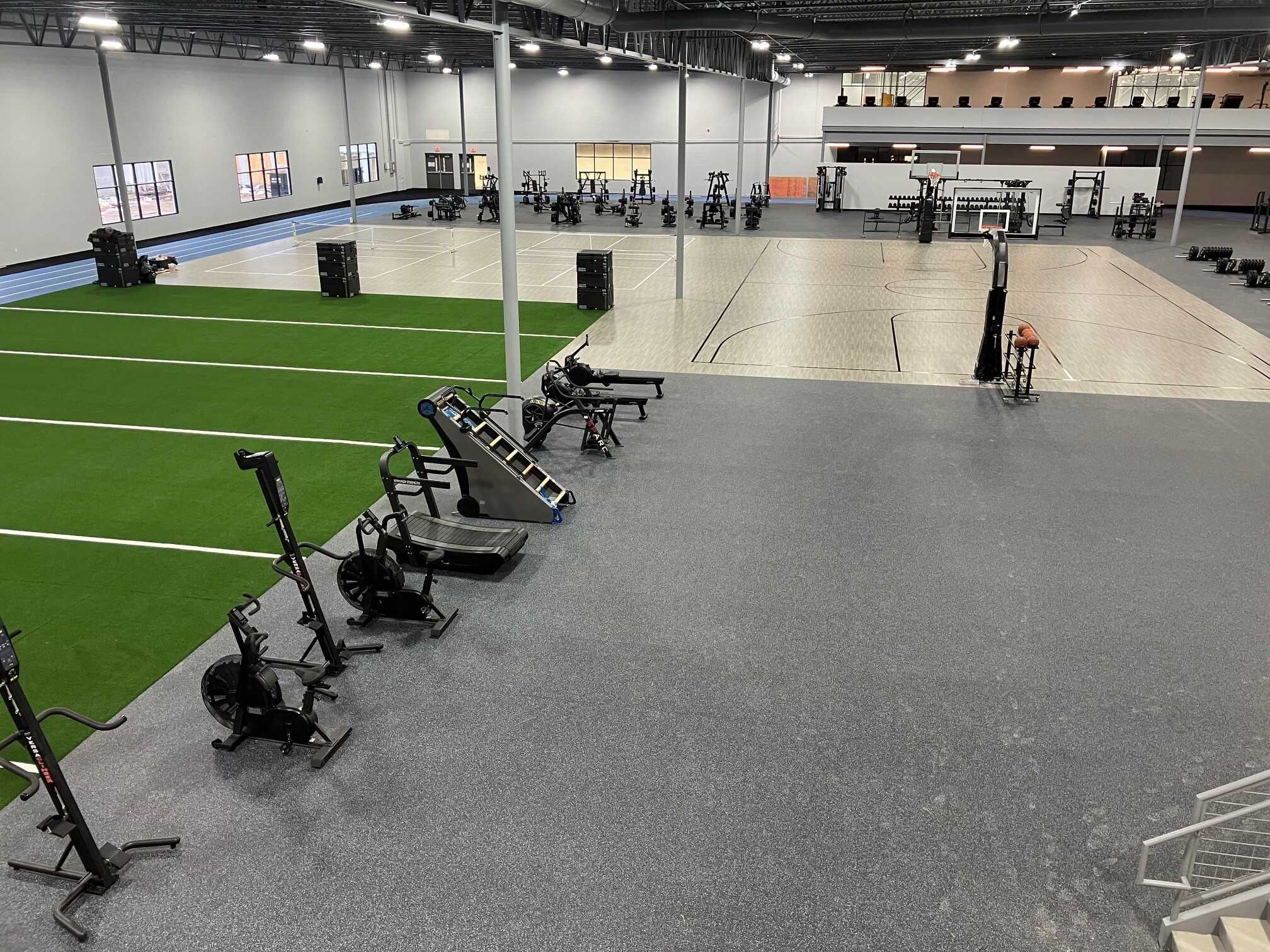 Modern fitness facility with weight equipment, turf area, and basketball court