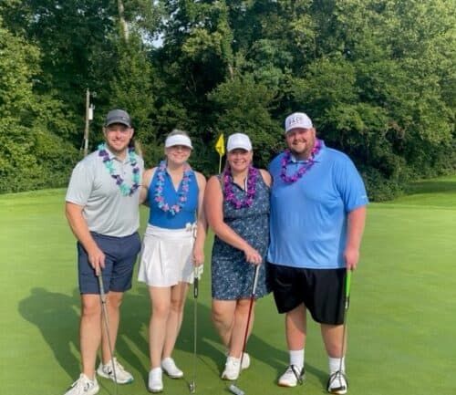 Four golfers wearing colorful leis posing together on golf course green